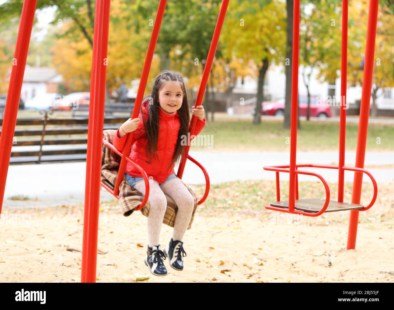 Little girl on swing in city park Stock Photo