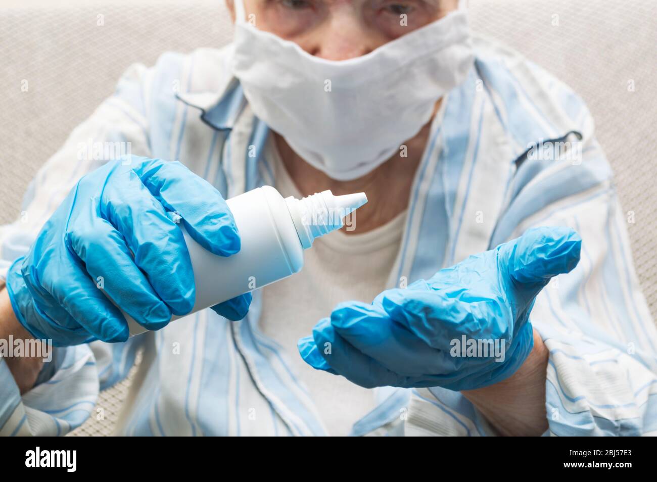 Hand disinfection and virus protection concept. Elderly woman sanitizing hands in rubber gloves squeeze alcohol from bottle Stock Photo