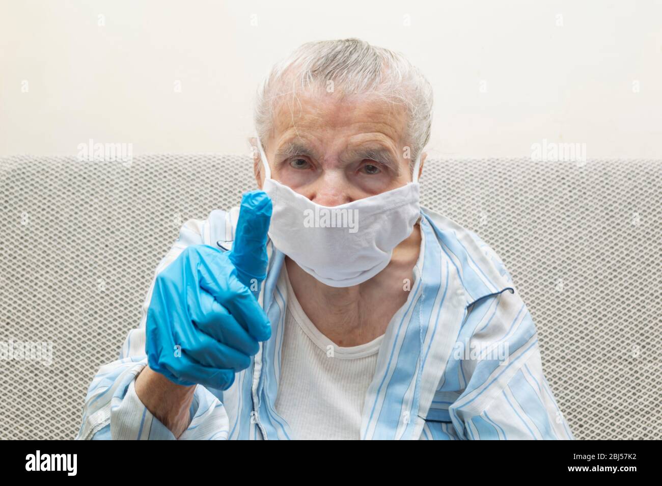 Elderly woman shows thumb up for fighting with COVID-19 by wearing hygiene mask and protective gloves. Coronavirus protection concept Stock Photo