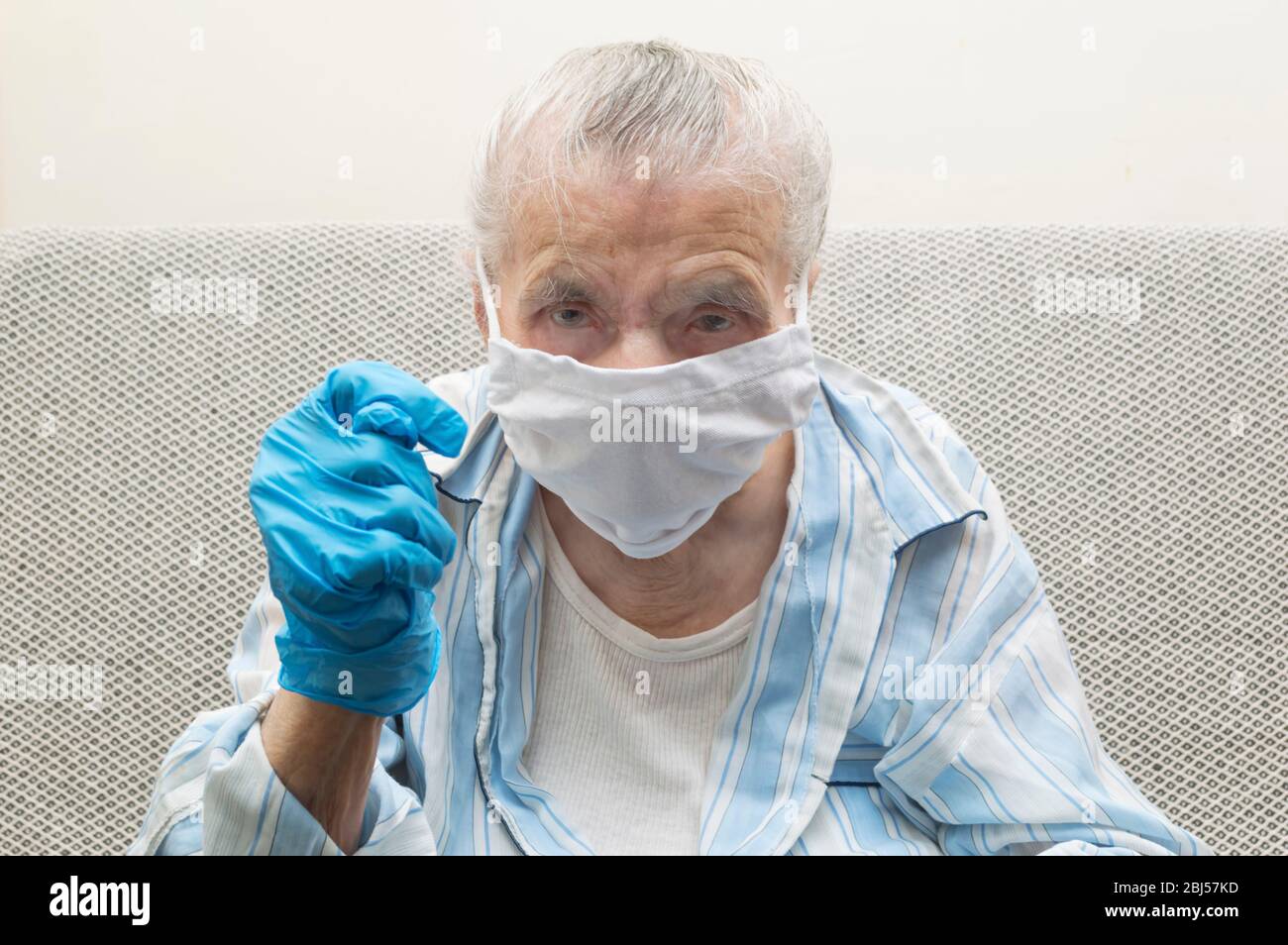 Elderly woman with a medical mask and raised hand showing a fig sign. She showing a fig sign to fight Covid-19 virus outbreak and pandemic around the Stock Photo