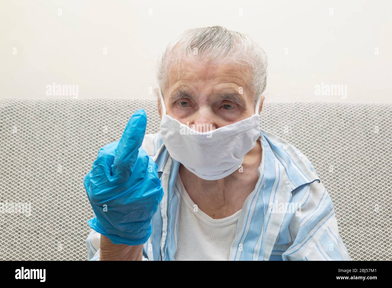 Elderly woman with a medical mask and raised hand showing middle finger. She showing a middle finger to fight Covid-19 virus outbreak and pandemic aro Stock Photo