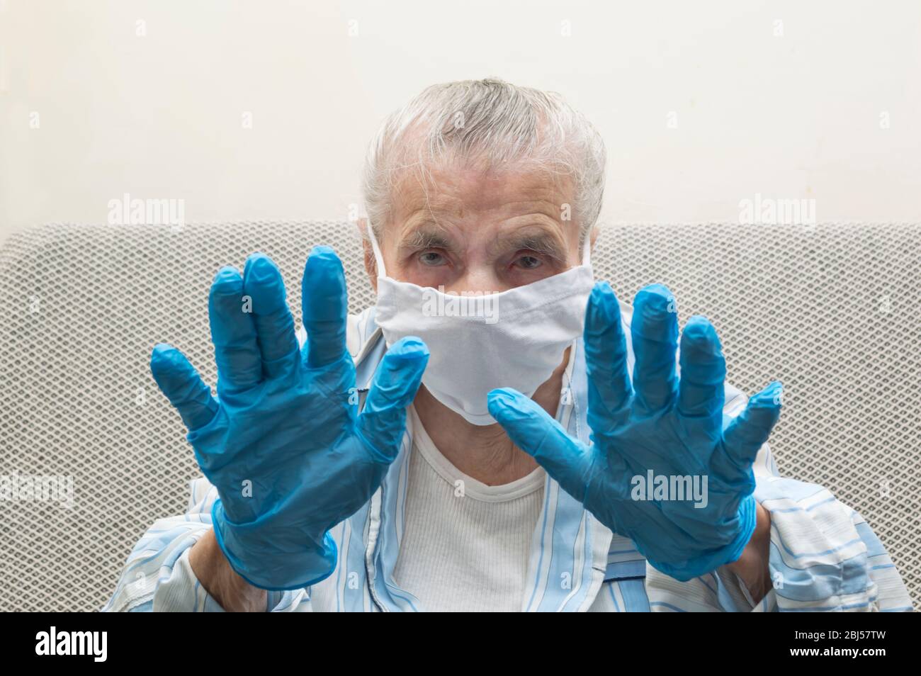 Elderly woman with a medical mask and raised hand in stop sign. She show stop hands to stop Covid-19 virus outbreak and pandemic around the world. Cor Stock Photo