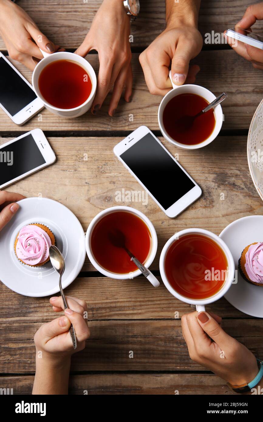 Four hands with smart phones holding cups with tea, on wooden table ...