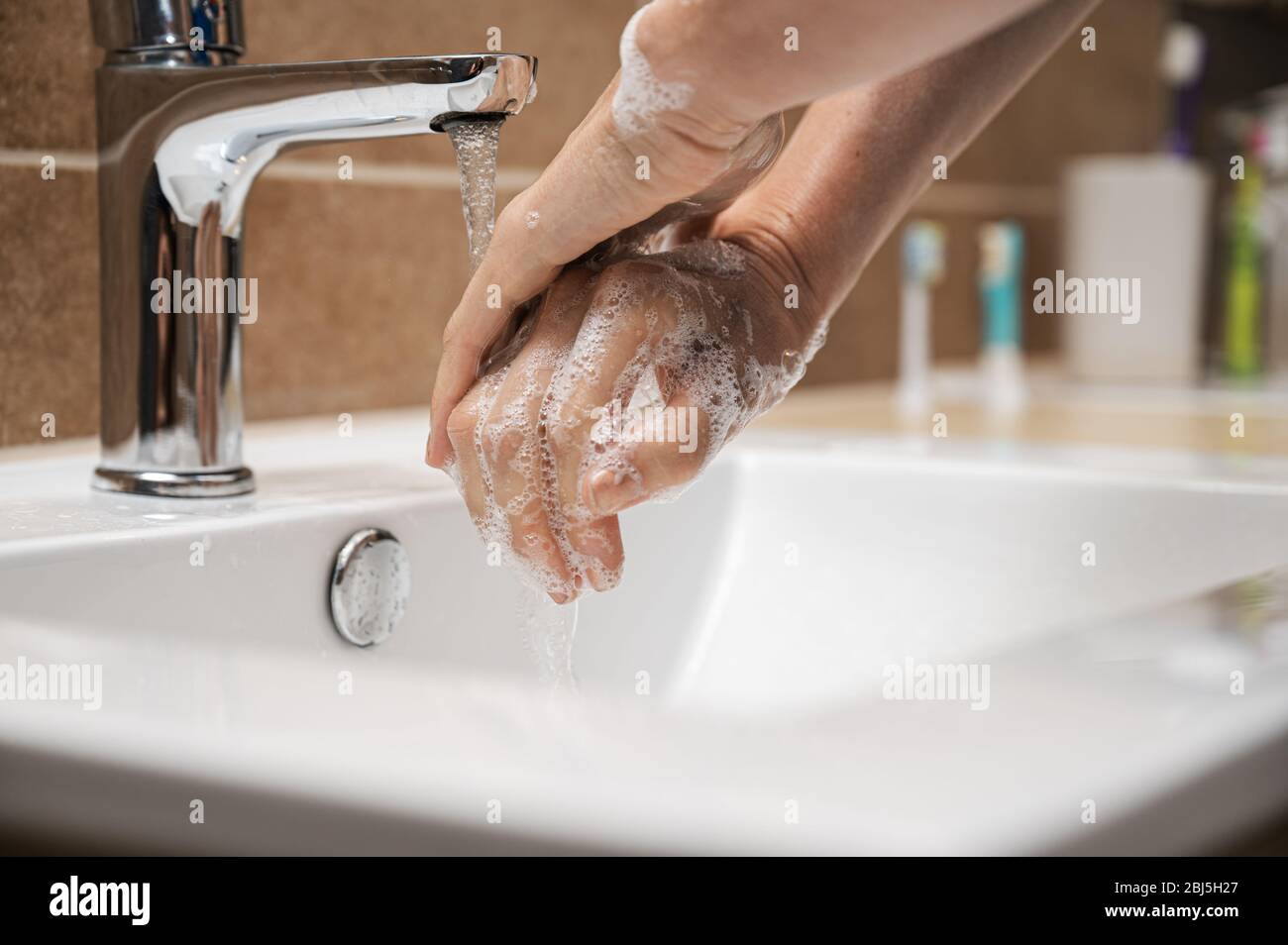 Low angle closeup view of woman washing her hands with soap under clean ...