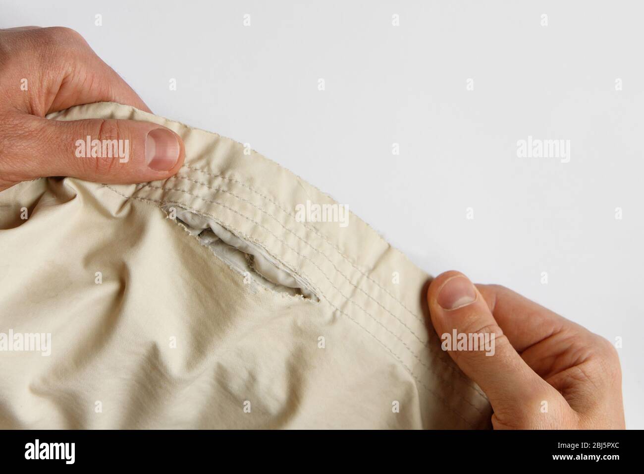 Man showing and holding white parka/jacket with worn to holes fabric