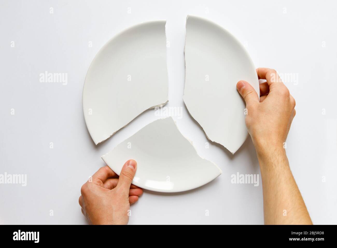 Top view of man hands holding a broken white plate. Metaphor for divorce, relationships, friendships, crack in marriage. Love is gone. Isolated on whi Stock Photo