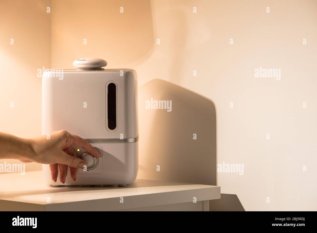 Female hand turn on aroma oil diffuser on the bedside table at night at home, steam from the air humidifier. Ultrasonic technology, increase in air hu Stock Photo