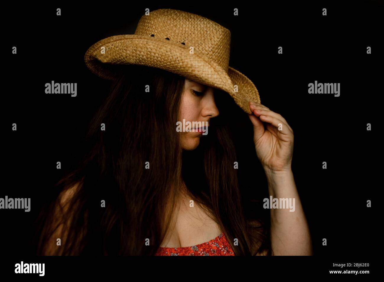 Sad lady in cowboy hat tipping her hat down in dramatic light Stock Photo