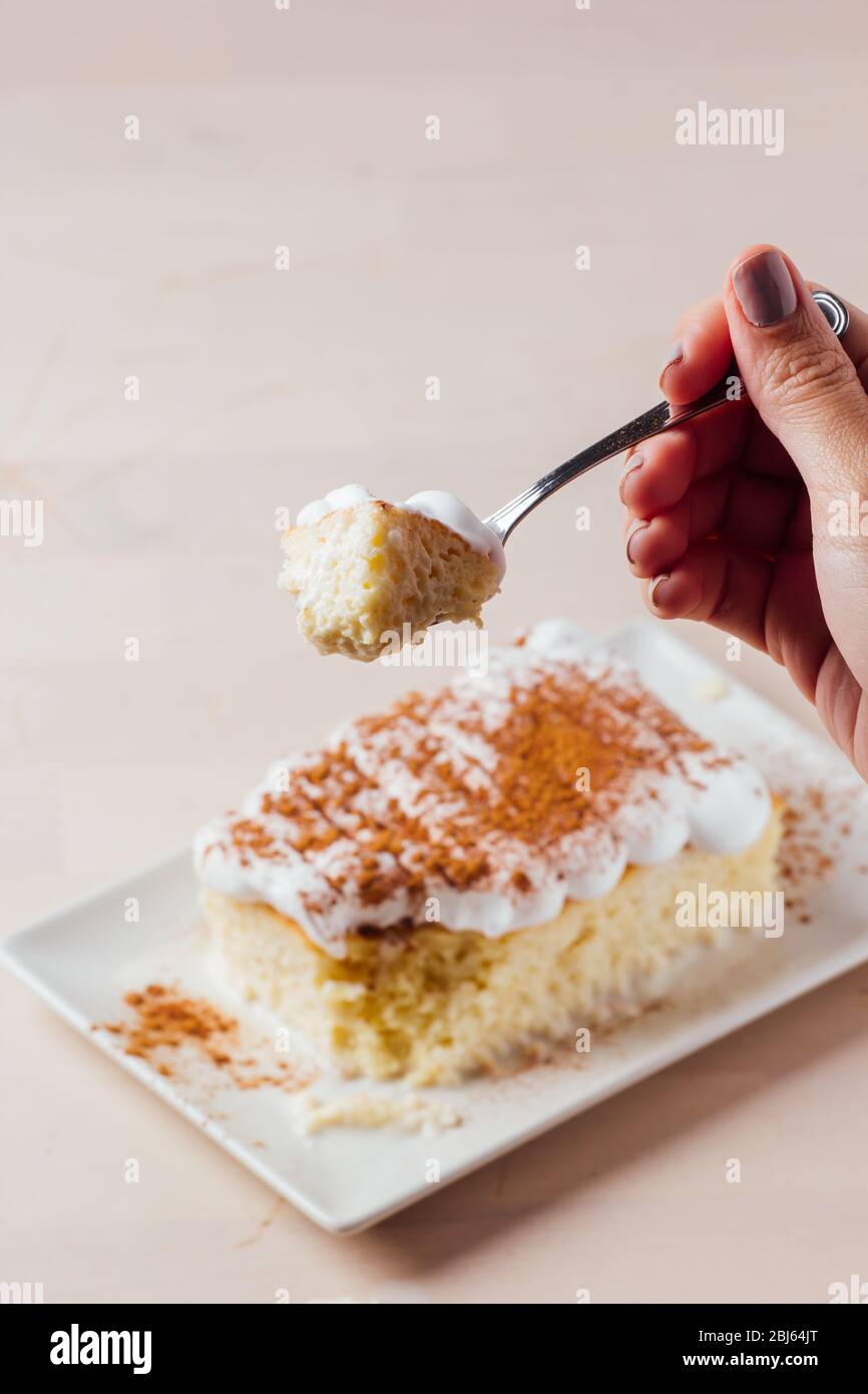 Woman's hand picking up a delicious piece of three milk cake, Latin American dessert Stock Photo