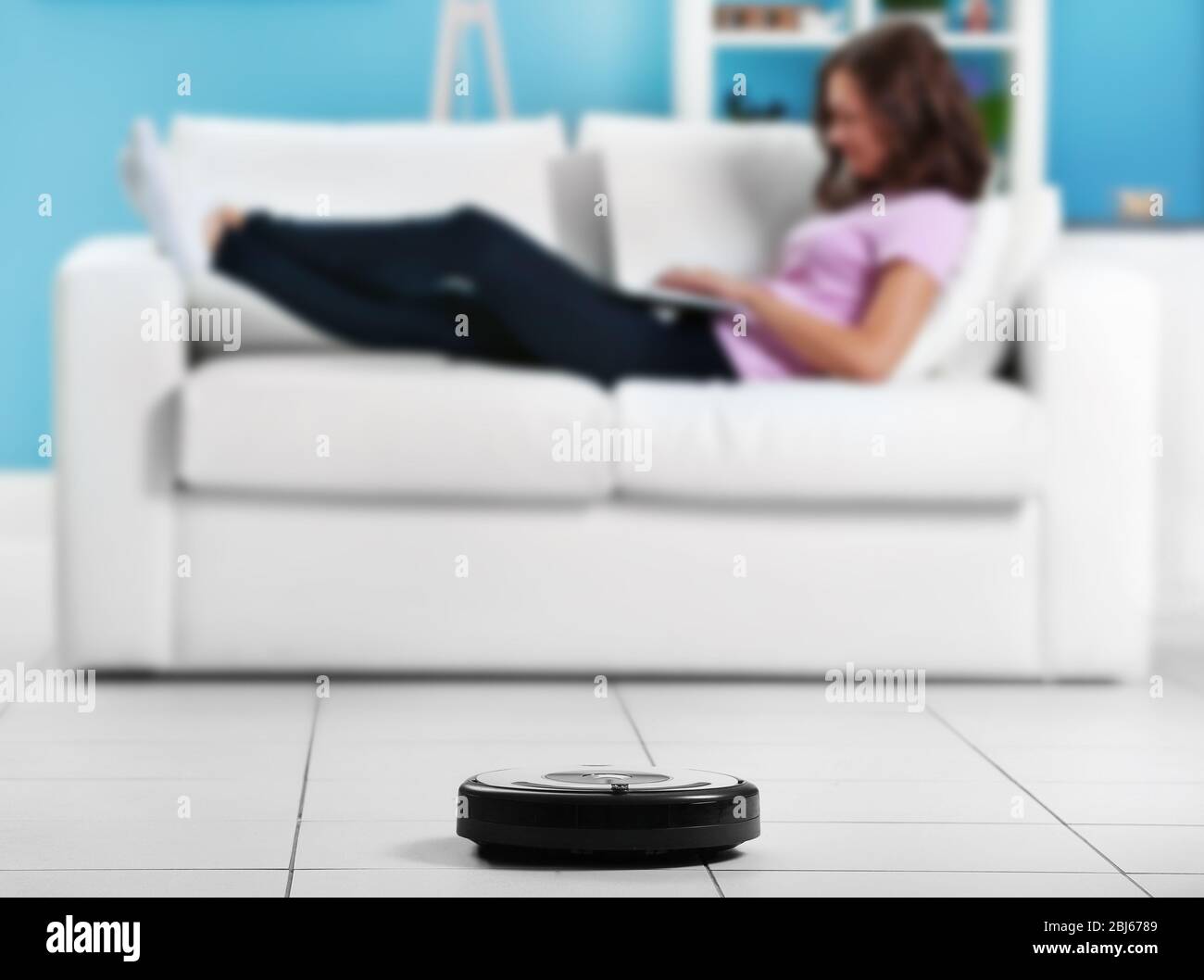 Cleaning concept - automatic robotic hoover clean the room while woman relaxing with laptop, close up Stock Photo