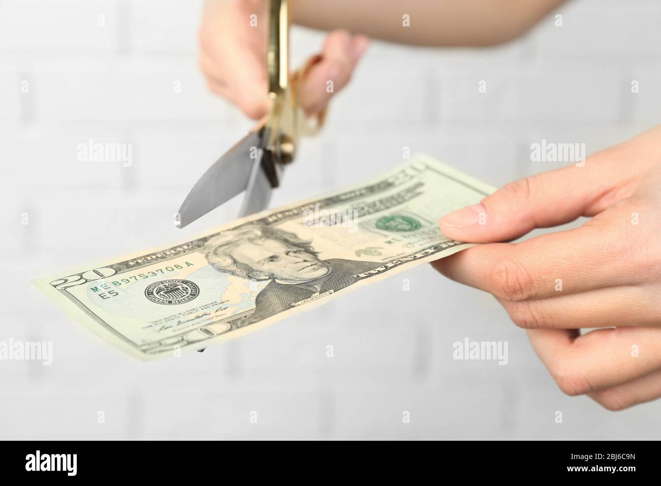 Hands with scissors cutting money on white brick wall background Stock