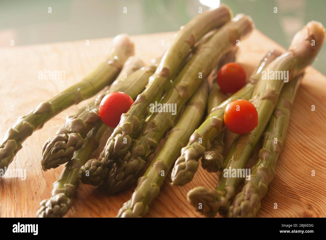 Largos tallos de espárragos verdes con tomates cherry alrededor listos para comerse en creudo Stock Photo