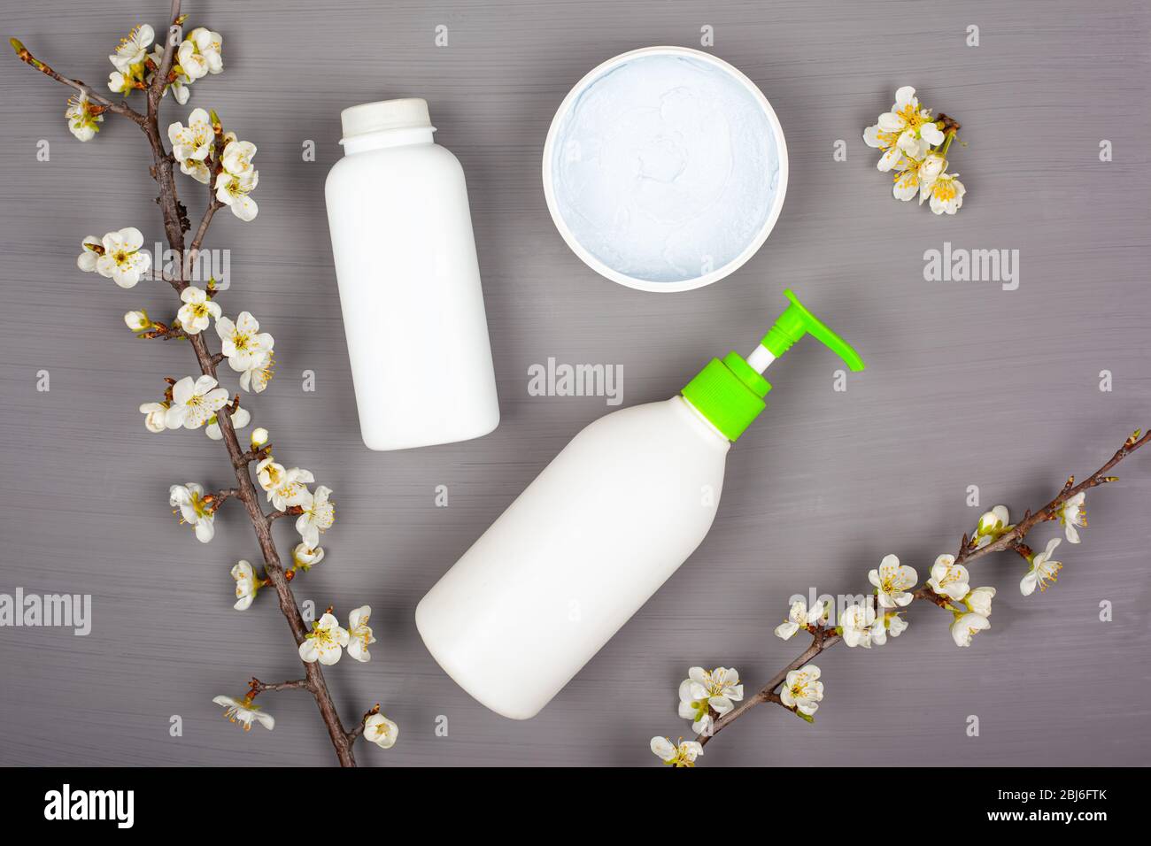 body care cosmetics, white bottles on a gray background with branches of blooming cherry, ,top view. Stock Photo