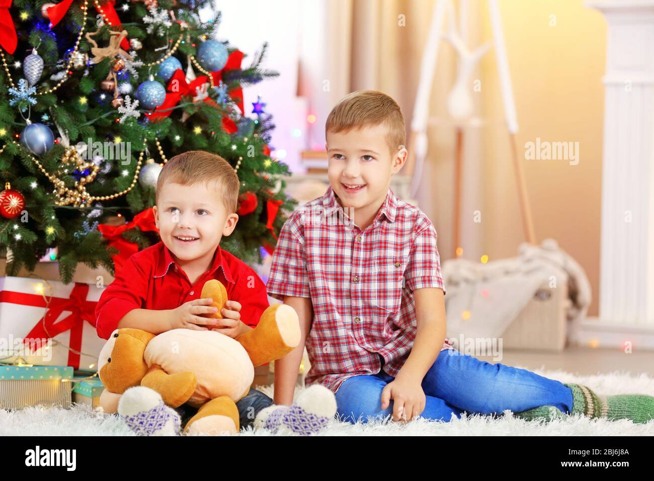 Two cute small brothers with teddy bear on Christmas tree background ...