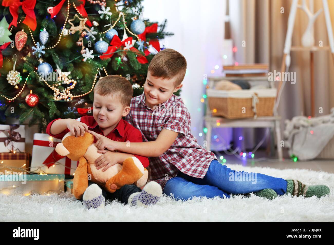 Two cute small brothers with teddy bear on Christmas tree background ...