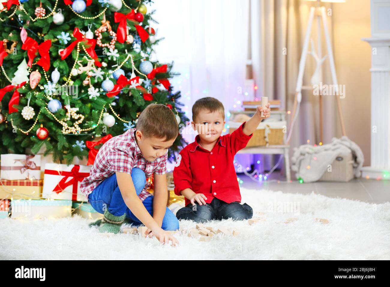 Two cute small brothers playing with wooden toys on Christmas tree ...