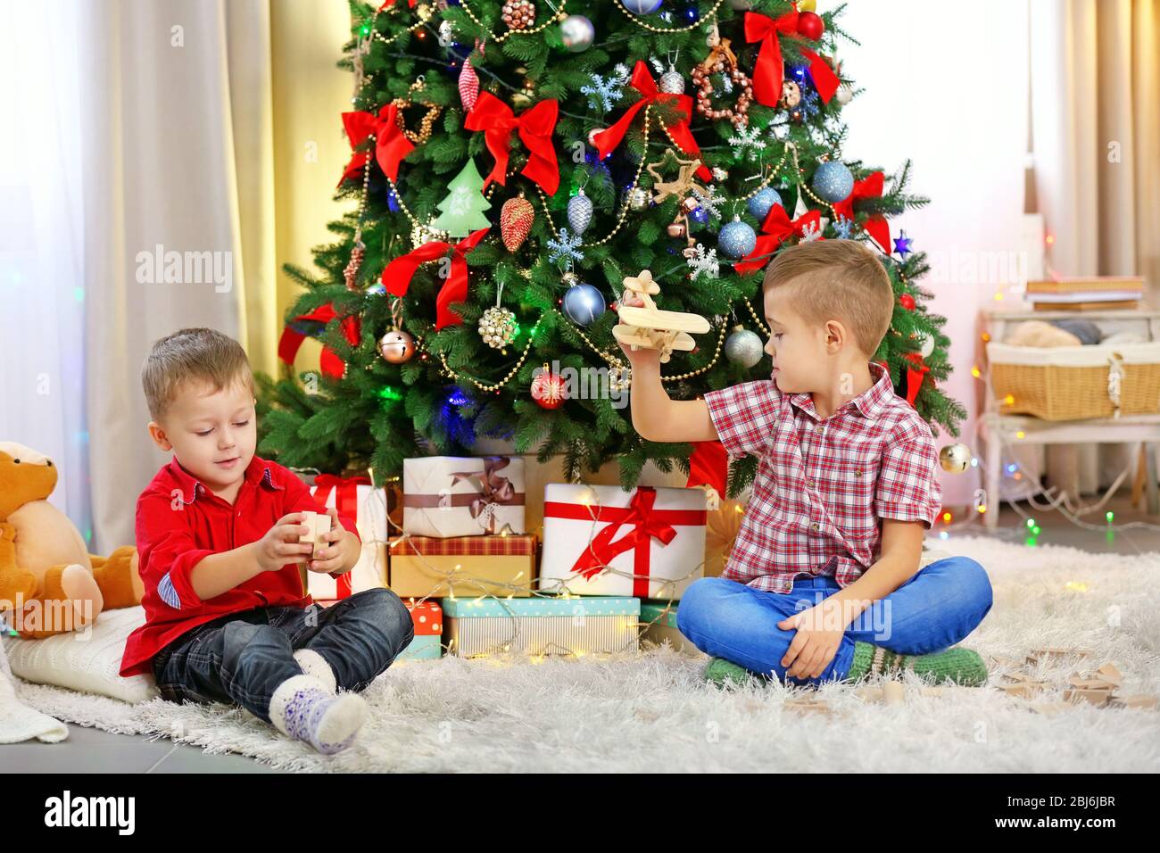 Two cute small brothers playing with wooden plane on Christmas tree ...