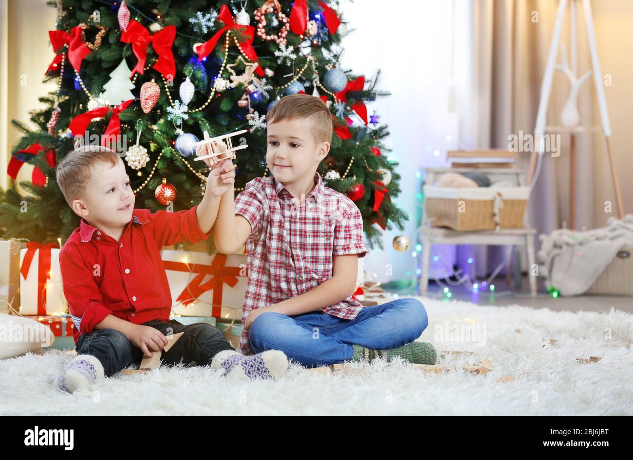 Two cute small brothers playing with wooden plane on Christmas tree ...