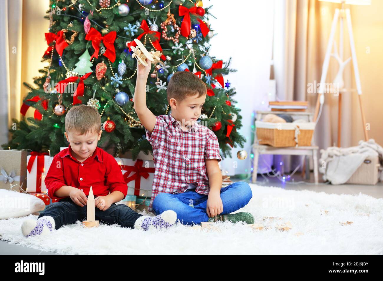 Two cute small brothers playing with wooden plane on Christmas tree ...