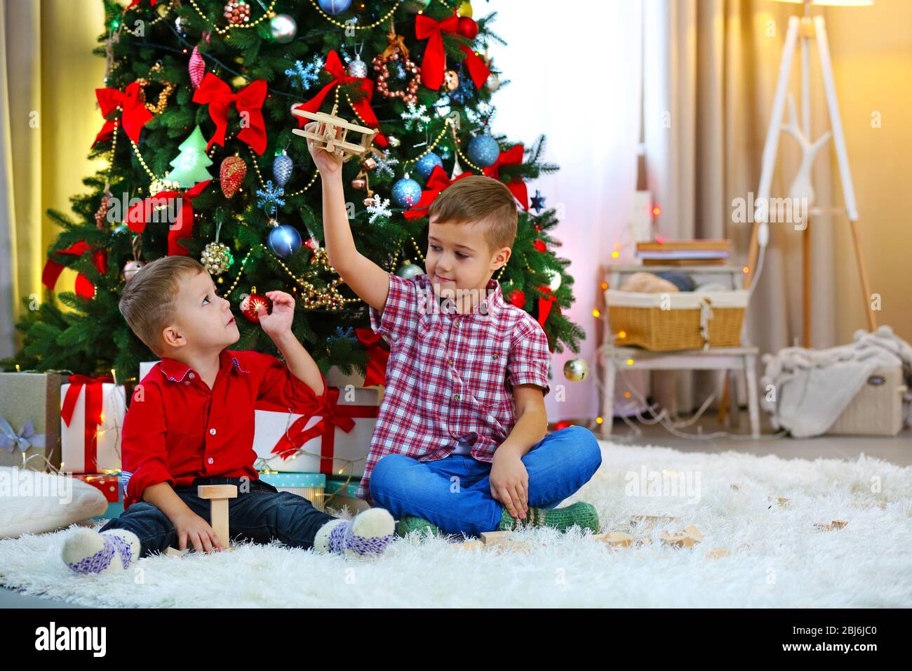 Two cute small brothers playing with wooden plane on Christmas tree ...