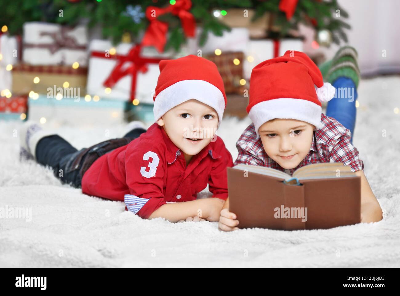Two cute small brothers reading book on Christmas decoration background ...