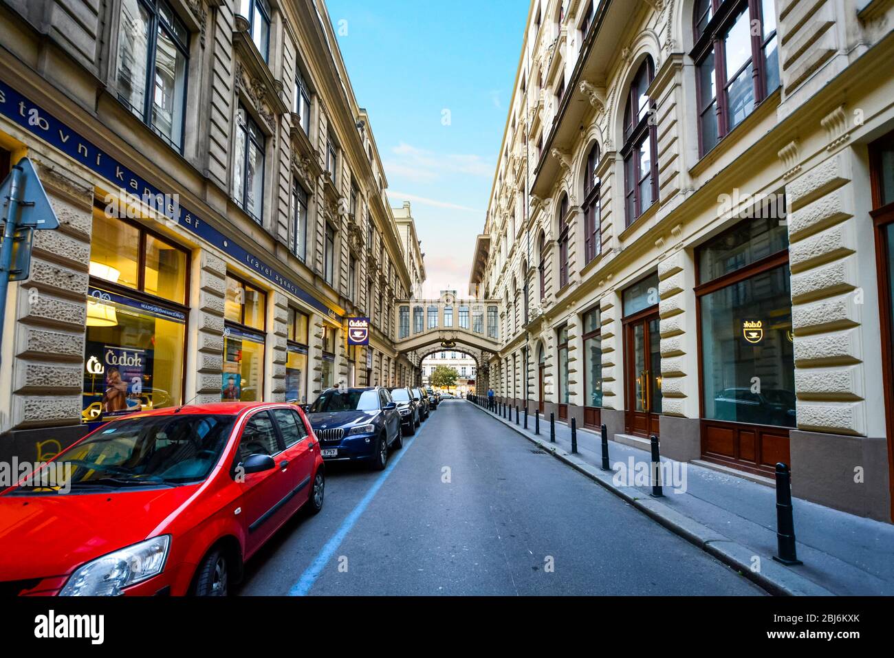 Cars park along a one way street with a pedestrian skyway bridge in view in the modern financial district of Budapest, Hungary. Stock Photo