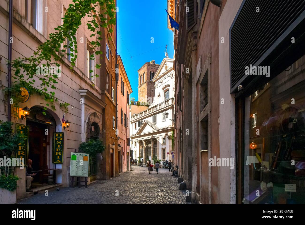 Two women walk down a shaded alley towards the Church of Sant' Eustachio with the head of a white stag holding it's cross in historic Rome, Italy. Stock Photo