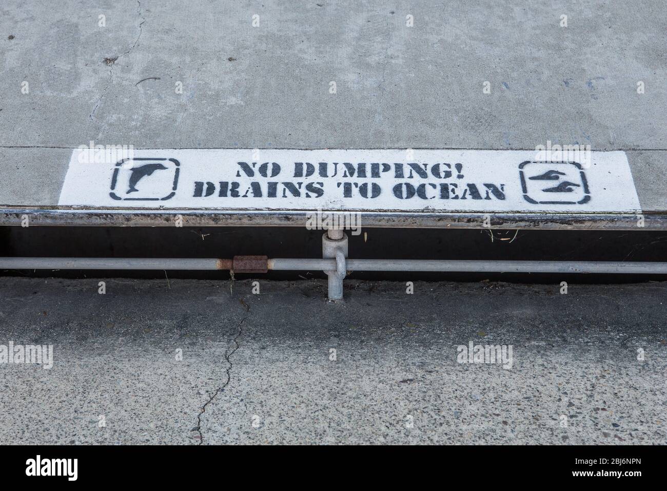 No dumping drains to ocean sign on the sidewalk over a street drain. Southern California USA Stock Photo