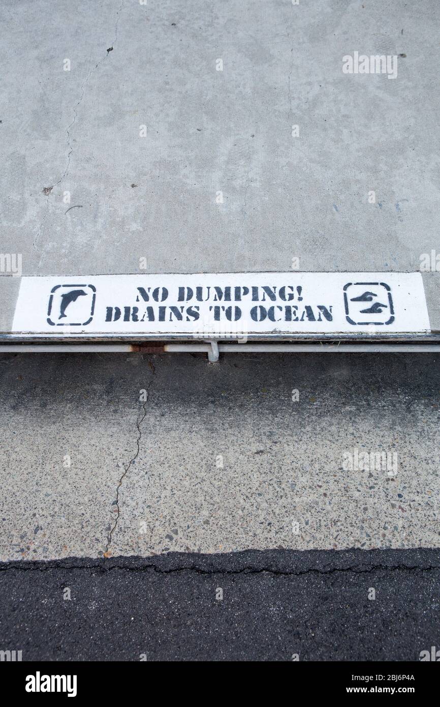 No dumping drains to ocean sign on the sidewalk over a street drain. Southern California USA Stock Photo