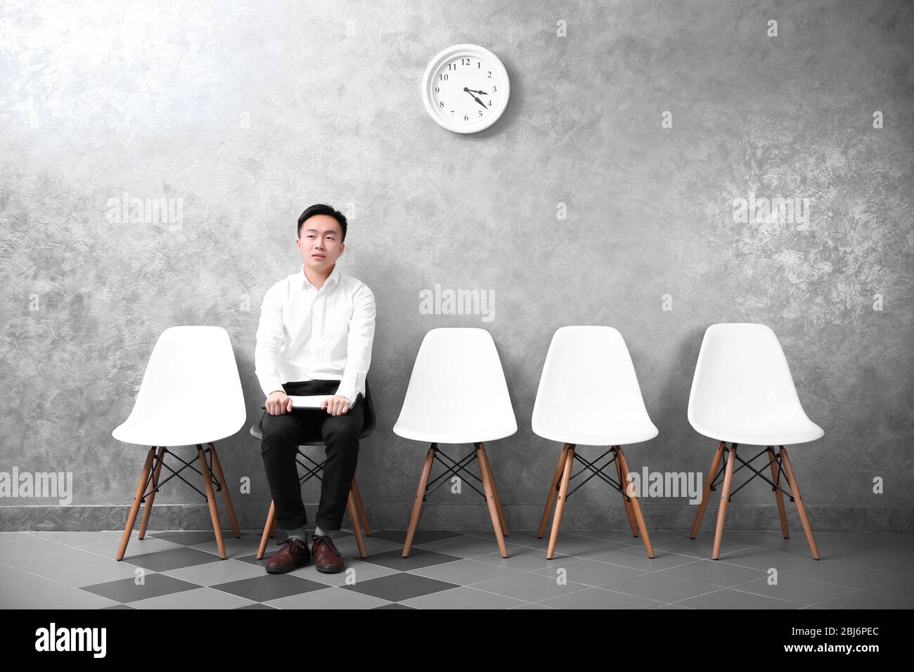 Young Asian businessman sitting on a chair in grey hall Stock Photo - Alamy