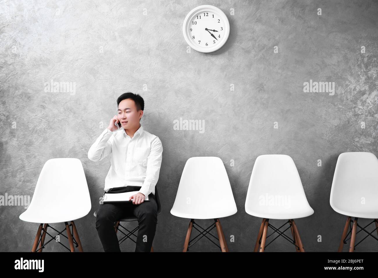 Young Asian businessman sitting on a chair in grey hall Stock Photo - Alamy