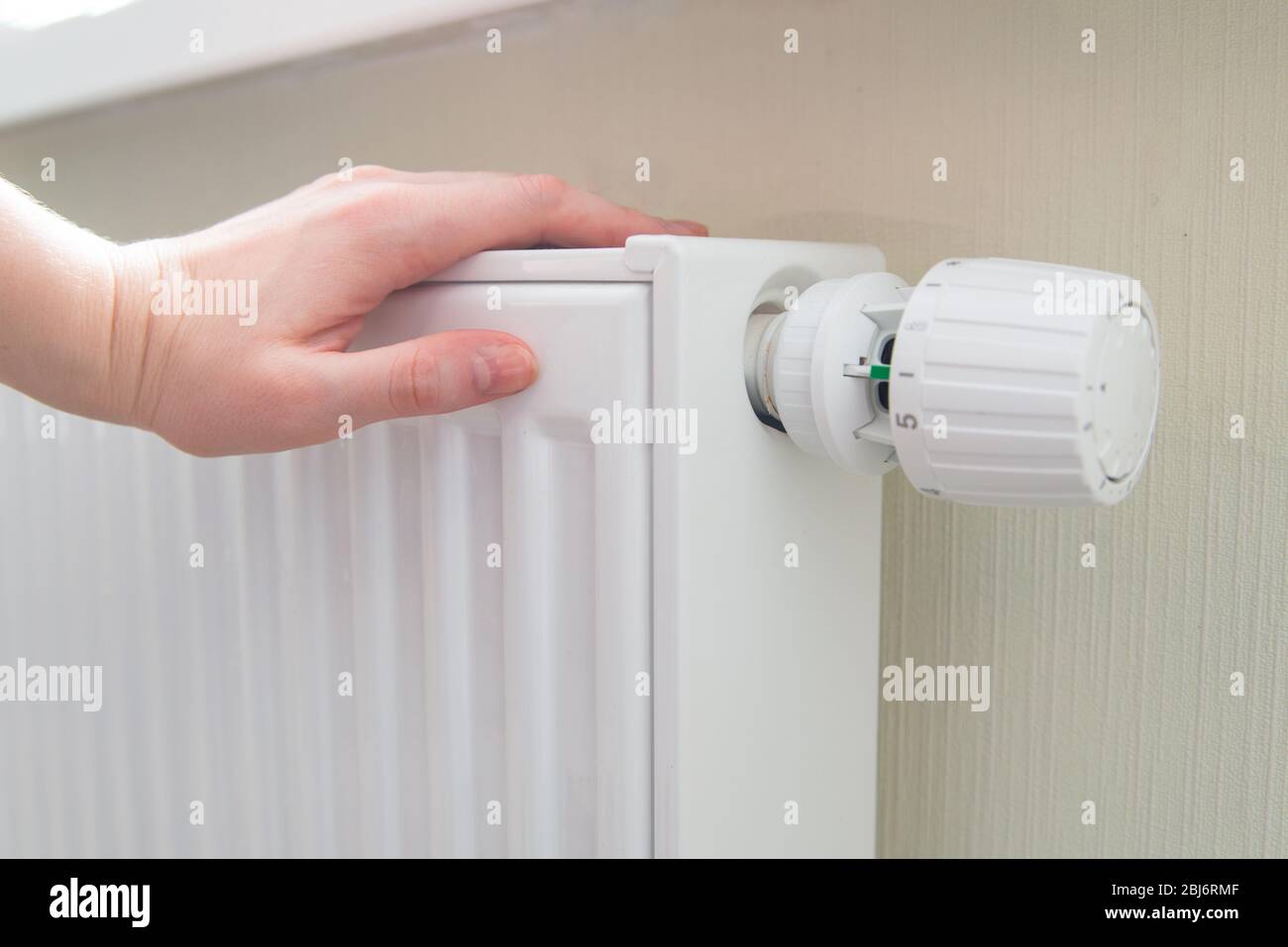 Home central heating system. Woman holds hand on the radiator Stock