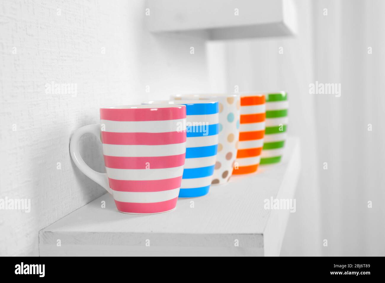 Set of striped cups on shelf against white wall background Stock Photo