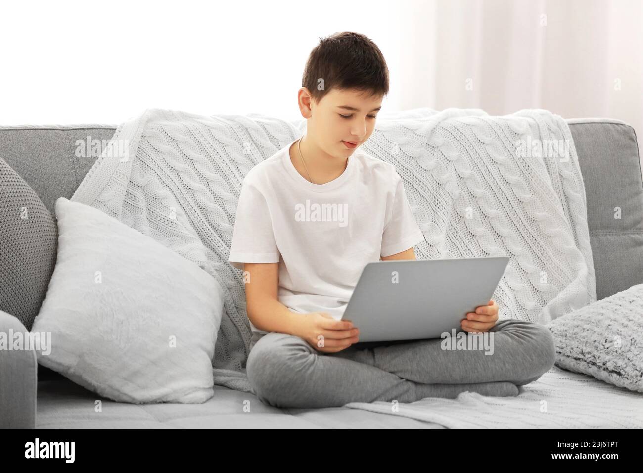 Boy using laptop on a sofa at home Stock Photo - Alamy