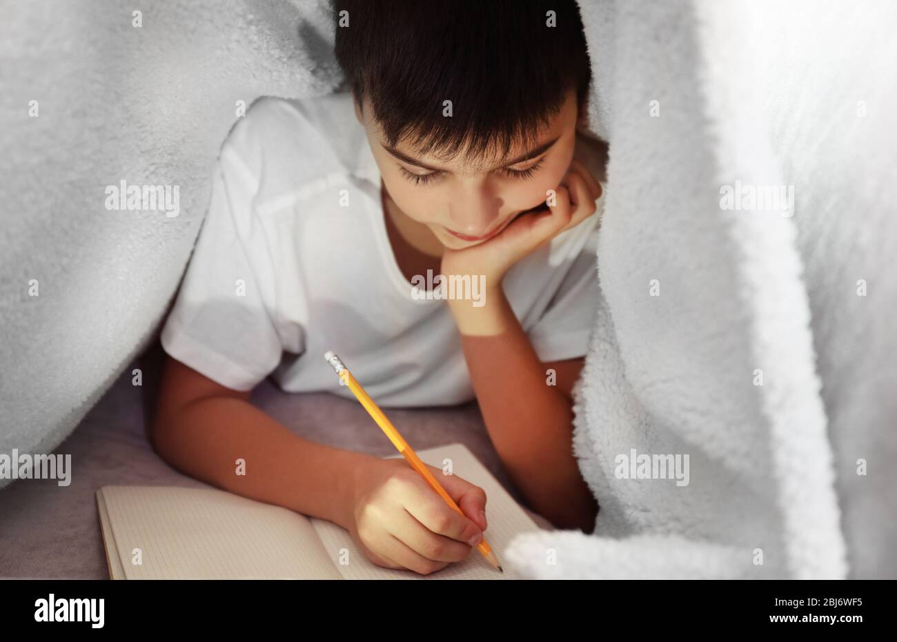 Little boy writing with pencil under the blanket Stock Photo