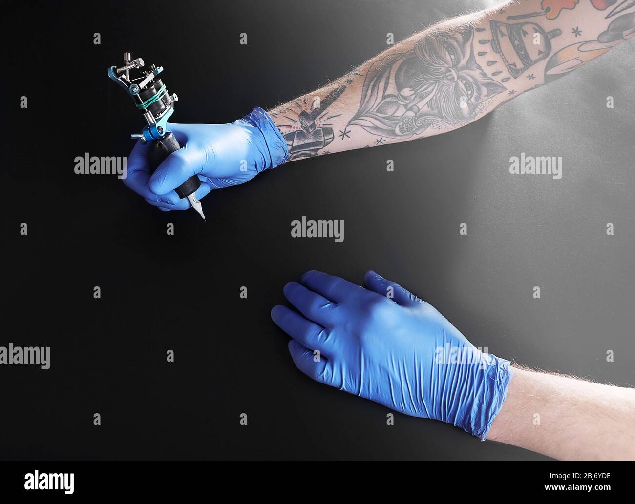 Tattooist hands in blue gloves with tattoo machine on black background Stock Photo - Alamy