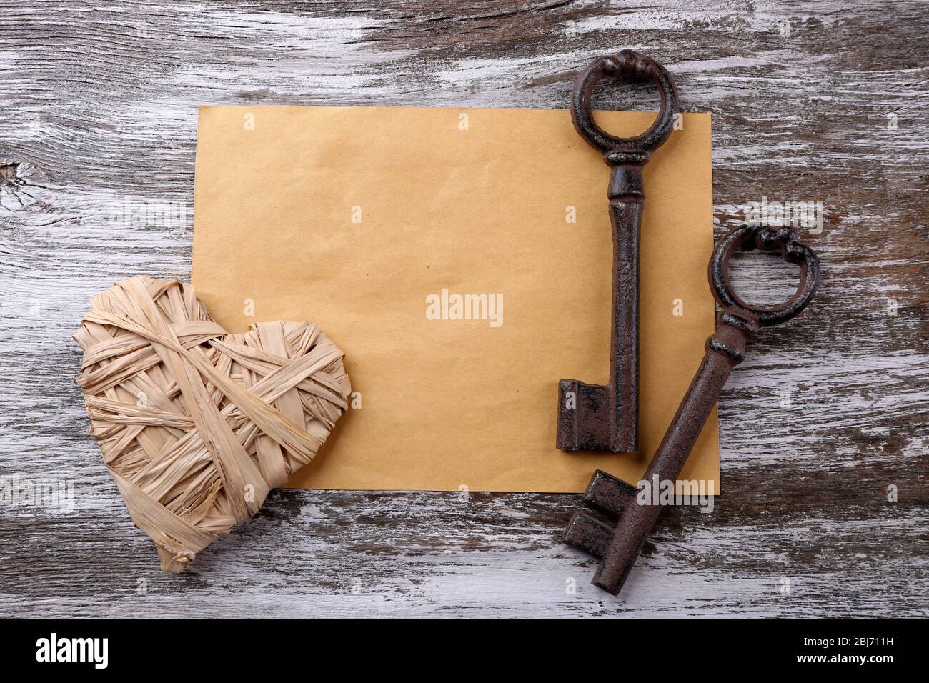 Old key with decorative heart and sheet of paper on grey wooden ...