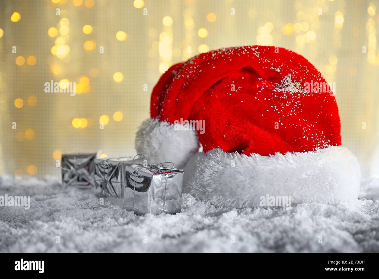 Santa Claus hat with gift boxes on a snowy table over glitter background Stock Photo