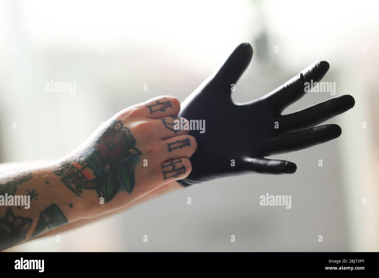 Man with tattoo wearing black latex gloves on blurred background Stock