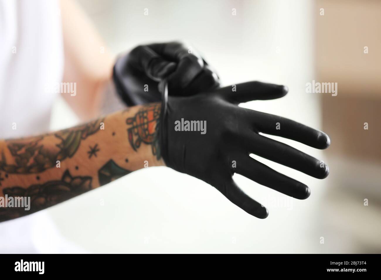 Man with tattoo wearing black latex gloves on blurred background Stock