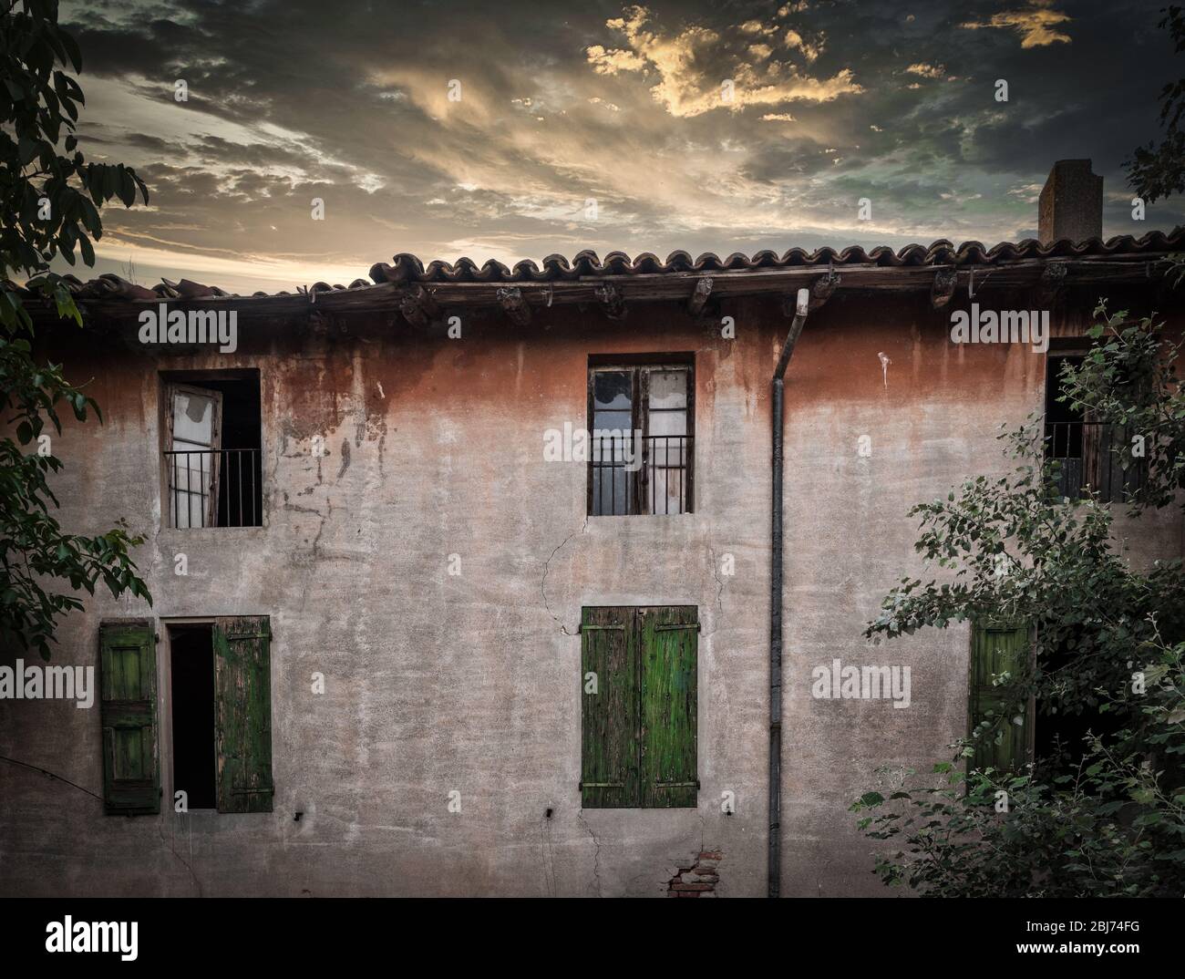 Rundown building with green shutters at sunset under stormy clouds outside of Bologna Italy Stock Photo