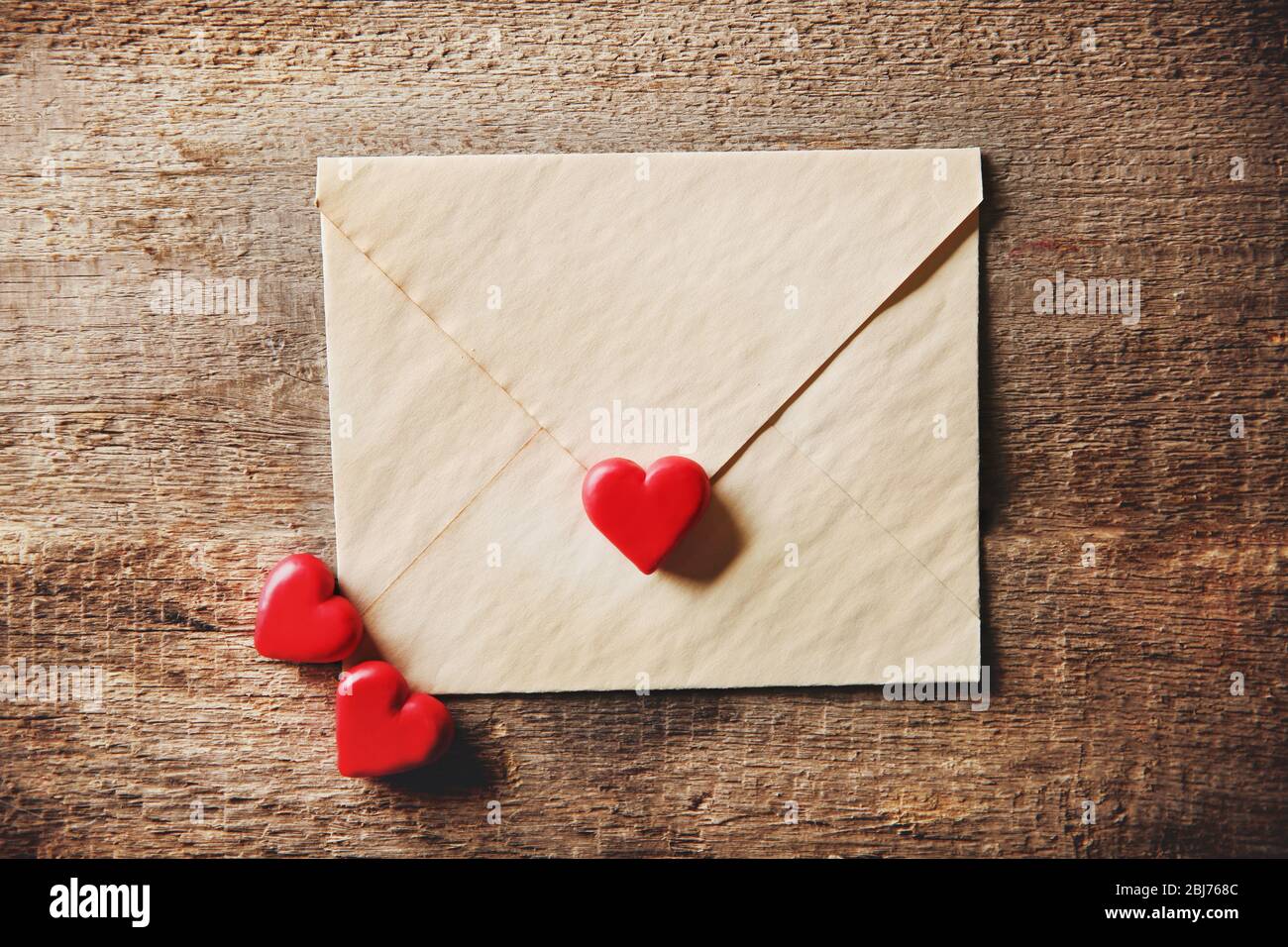 Old textured gift envelope with small heart on wooden background Stock Photo