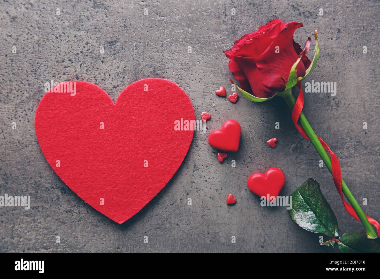 Beautiful red rose with small hearts on grey textured background Stock ...