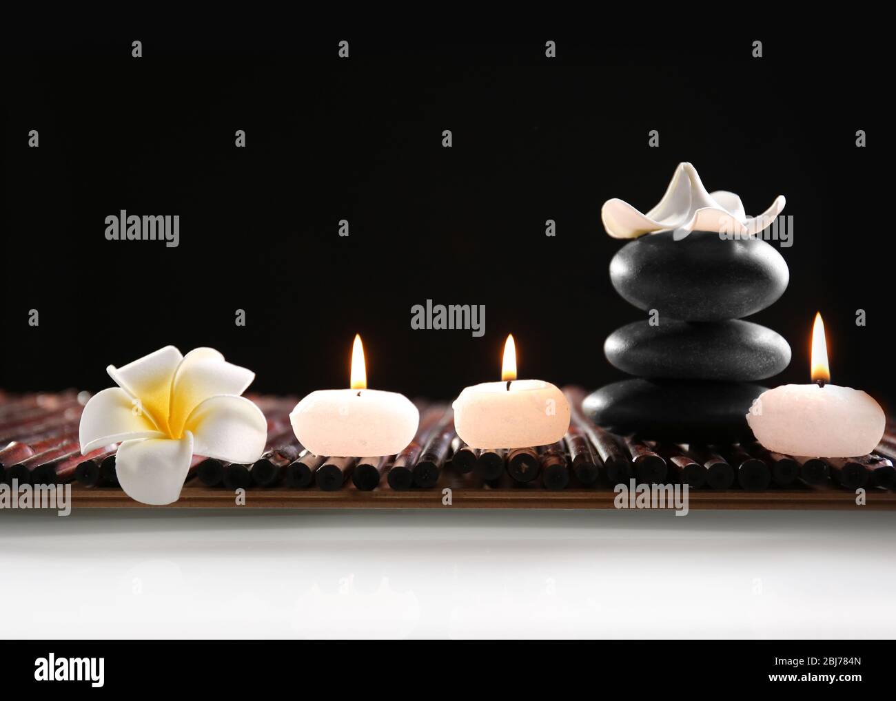 Spa still life with stones, candles and flowers in water on black ...