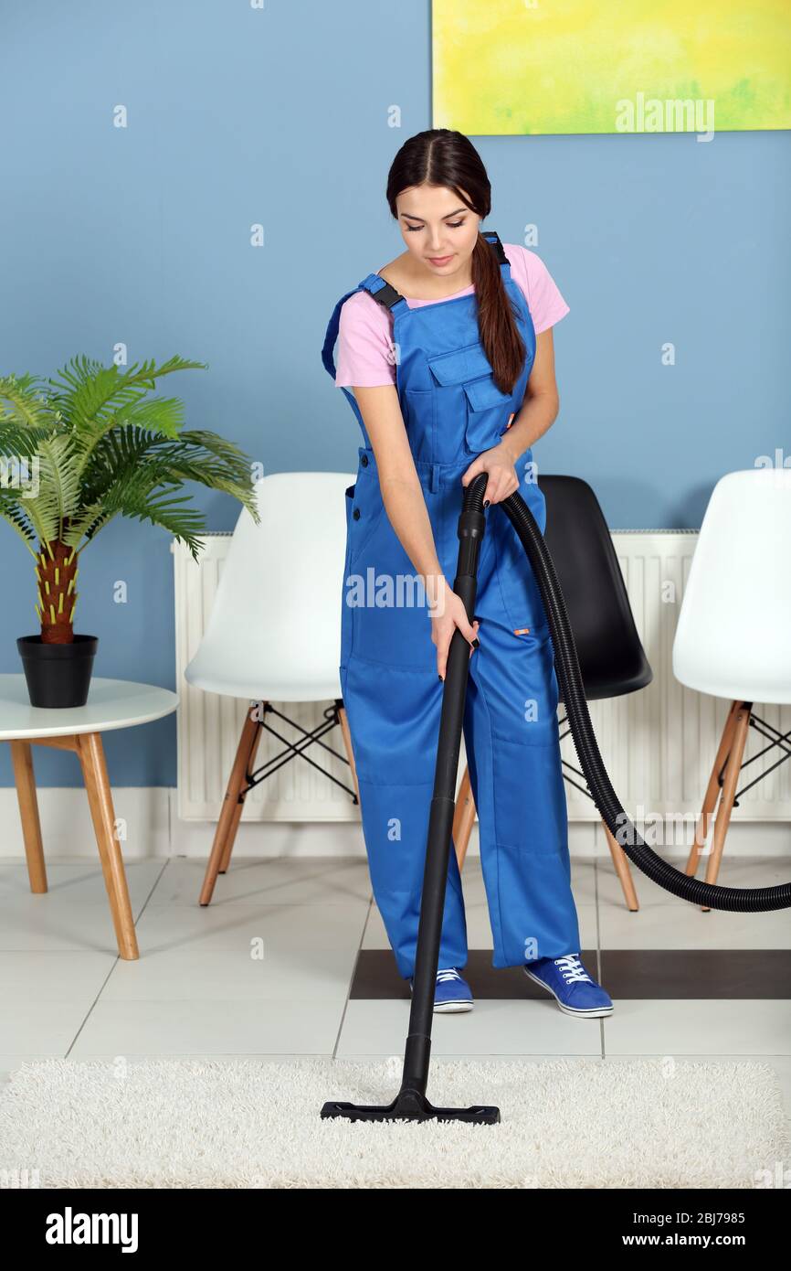 A pretty young woman in uniform vacuuming the floor at the office Stock ...
