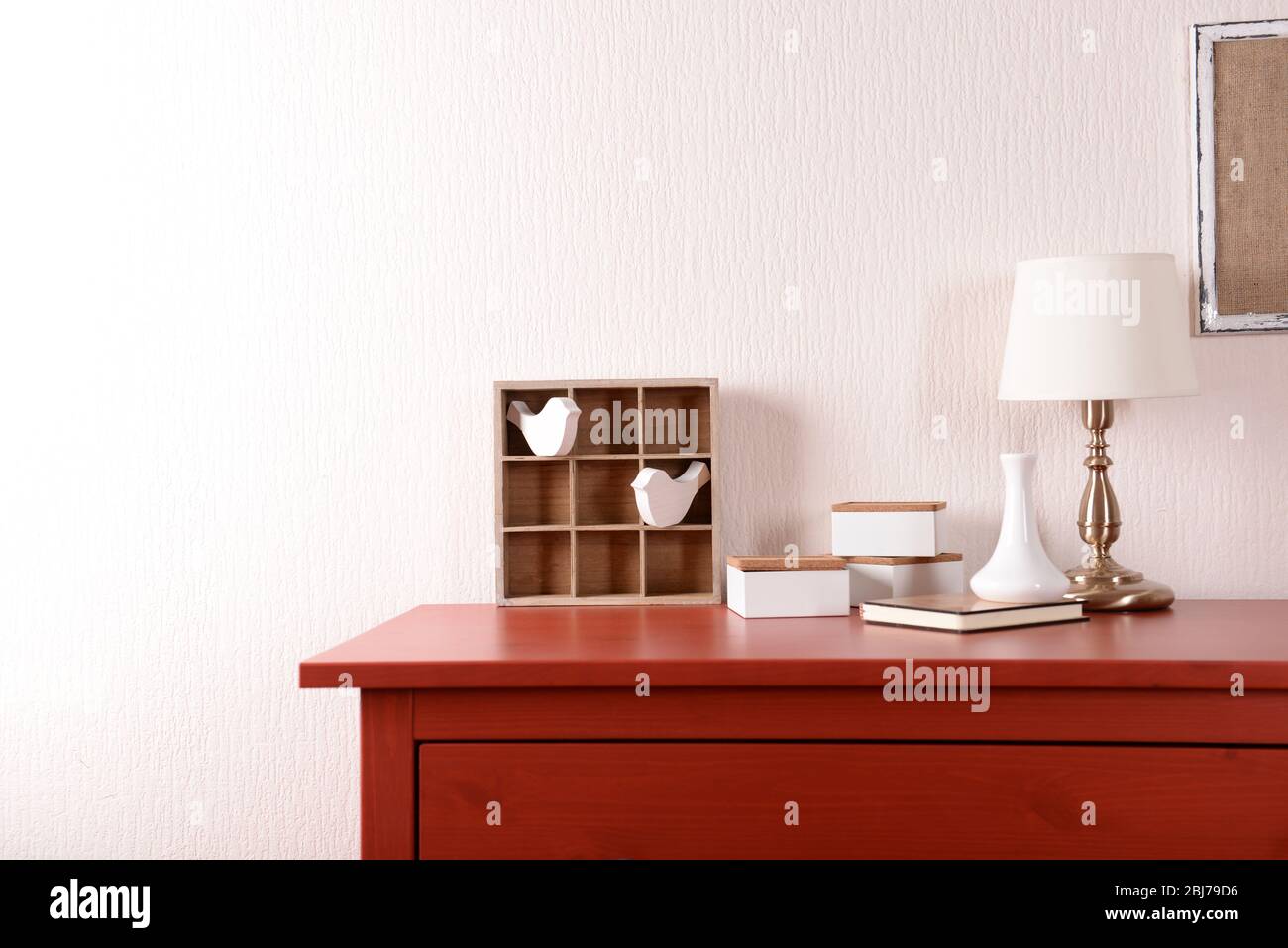 Room interior with red wooden commode, frame and lamp on light wall ...