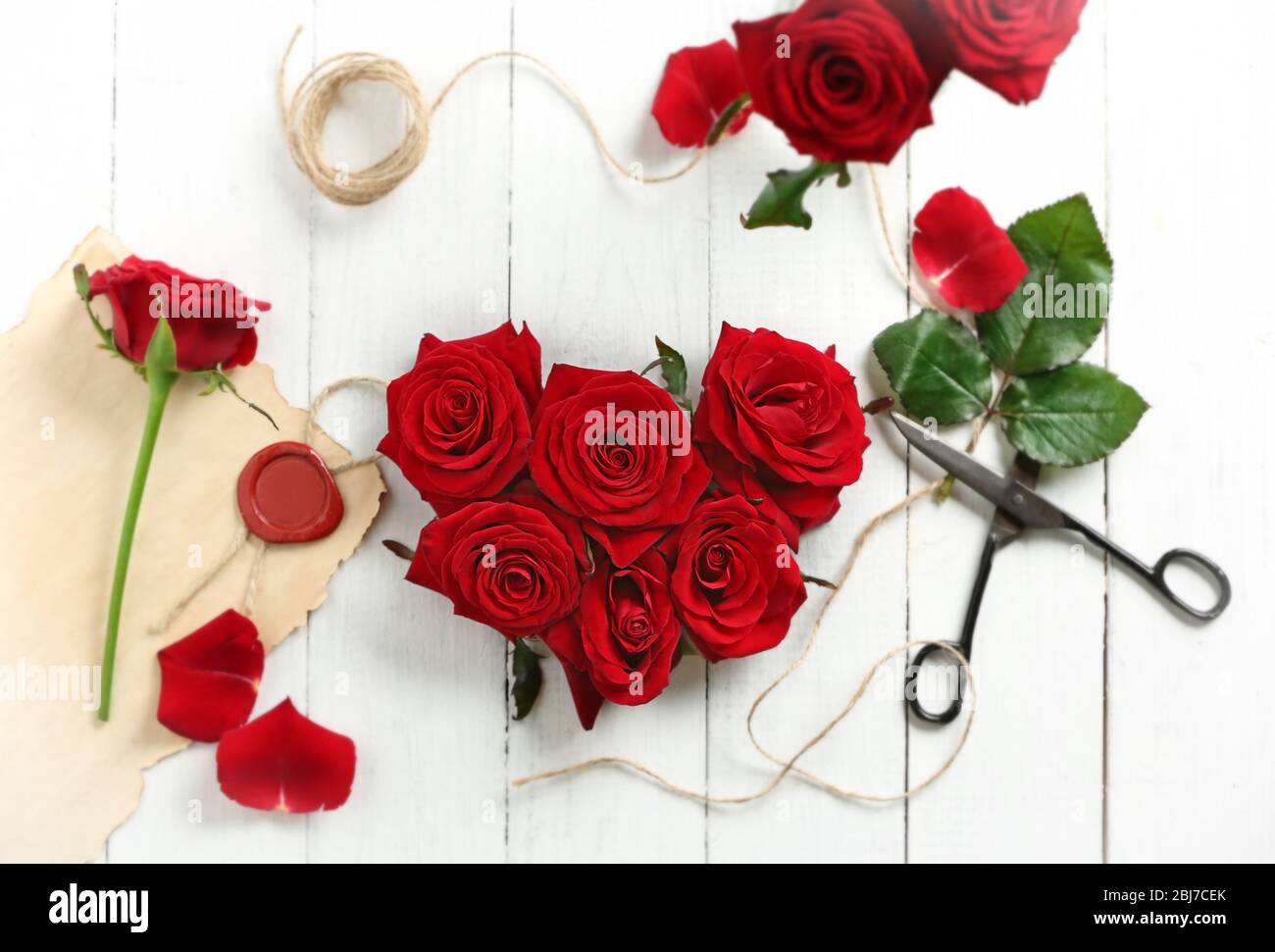 Fresh red roses buds in shape of heart with rope and scissors on wooden ...