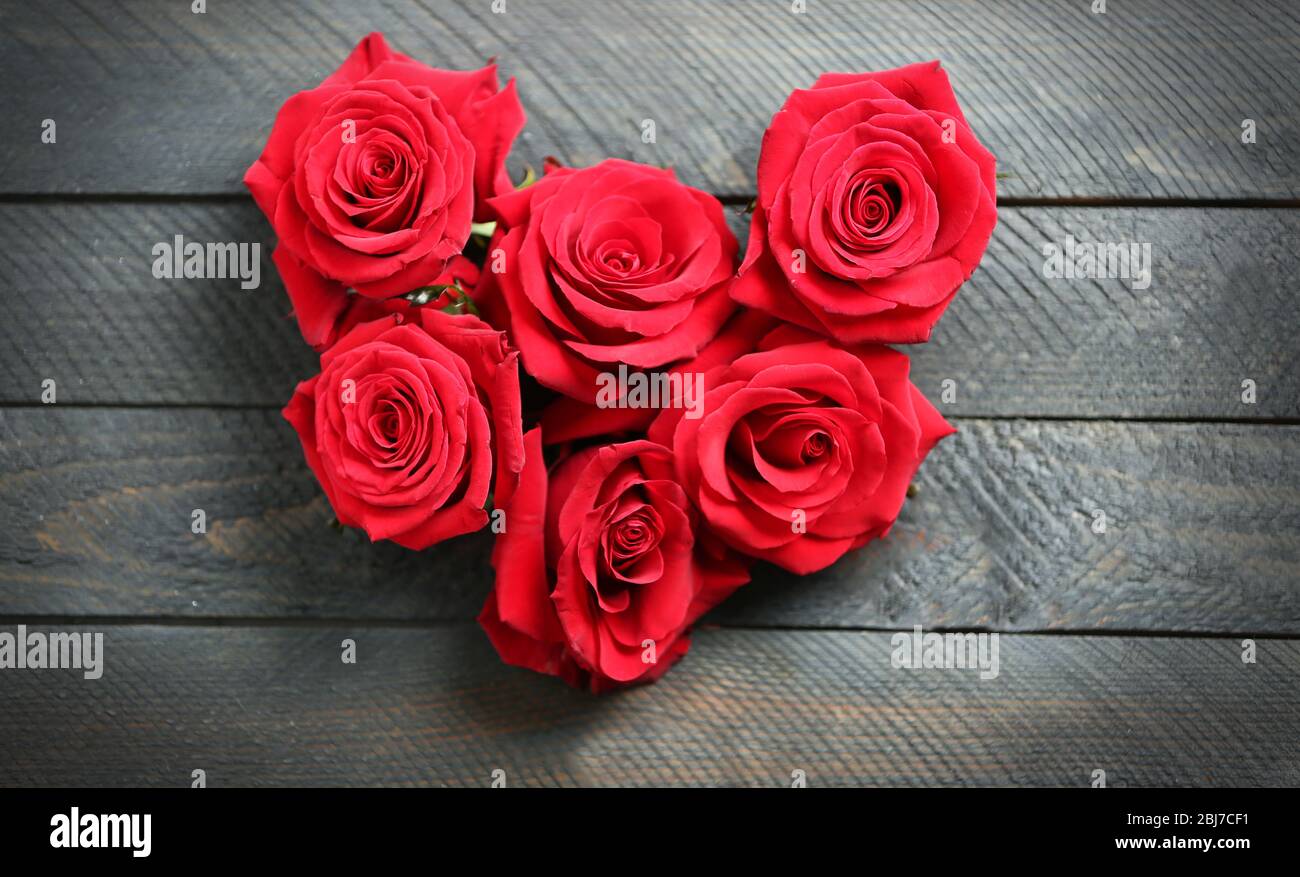 Fresh red roses buds in shape of heart on wooden background Stock Photo ...