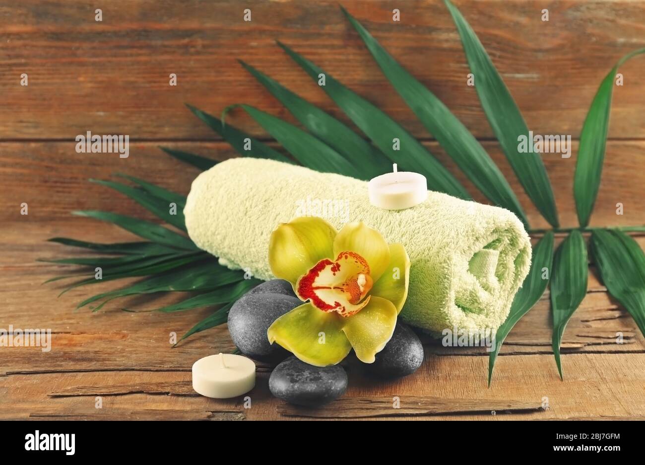 Spa stones with beautiful flowers, towel and candles on wooden background Stock Photo