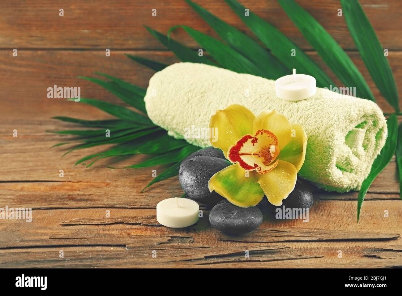 Spa stones with beautiful flowers, towel and candles on wooden background Stock Photo